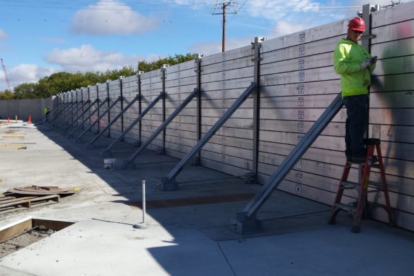A worker prepares to install a hold-down clamp, the final component of this flood wall project. The clamps exert downward pressure on the flood planks and compresses the horizontal plank gaskets.