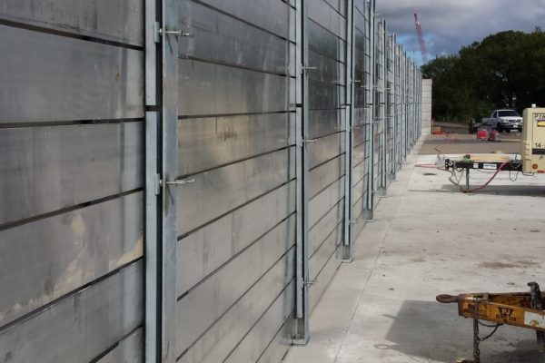 The completely installed flood barrier is seen from the wet side of the wall. The compression channels, which can be seen between the stoplogs and the posts, are adjusted to compress the vertical gaskets on the dry side of the posts, creating the watertight seal.